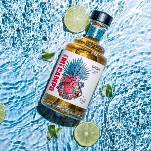 Mi Camp Reposado Tequila bottle flat shot on water background with limes 