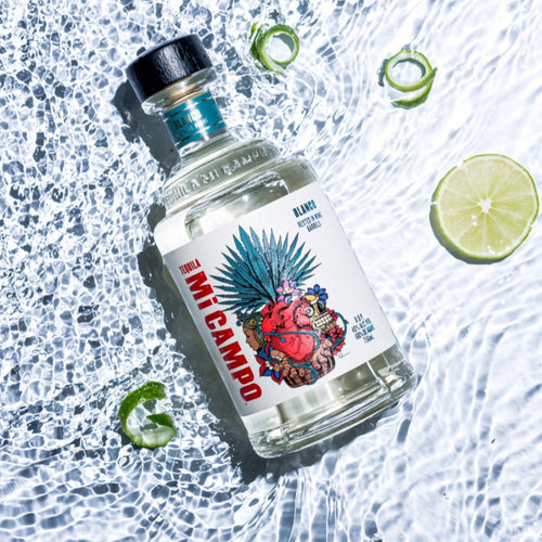 Mi Camp Blanco Tequila bottle flat shot on water background with limes 